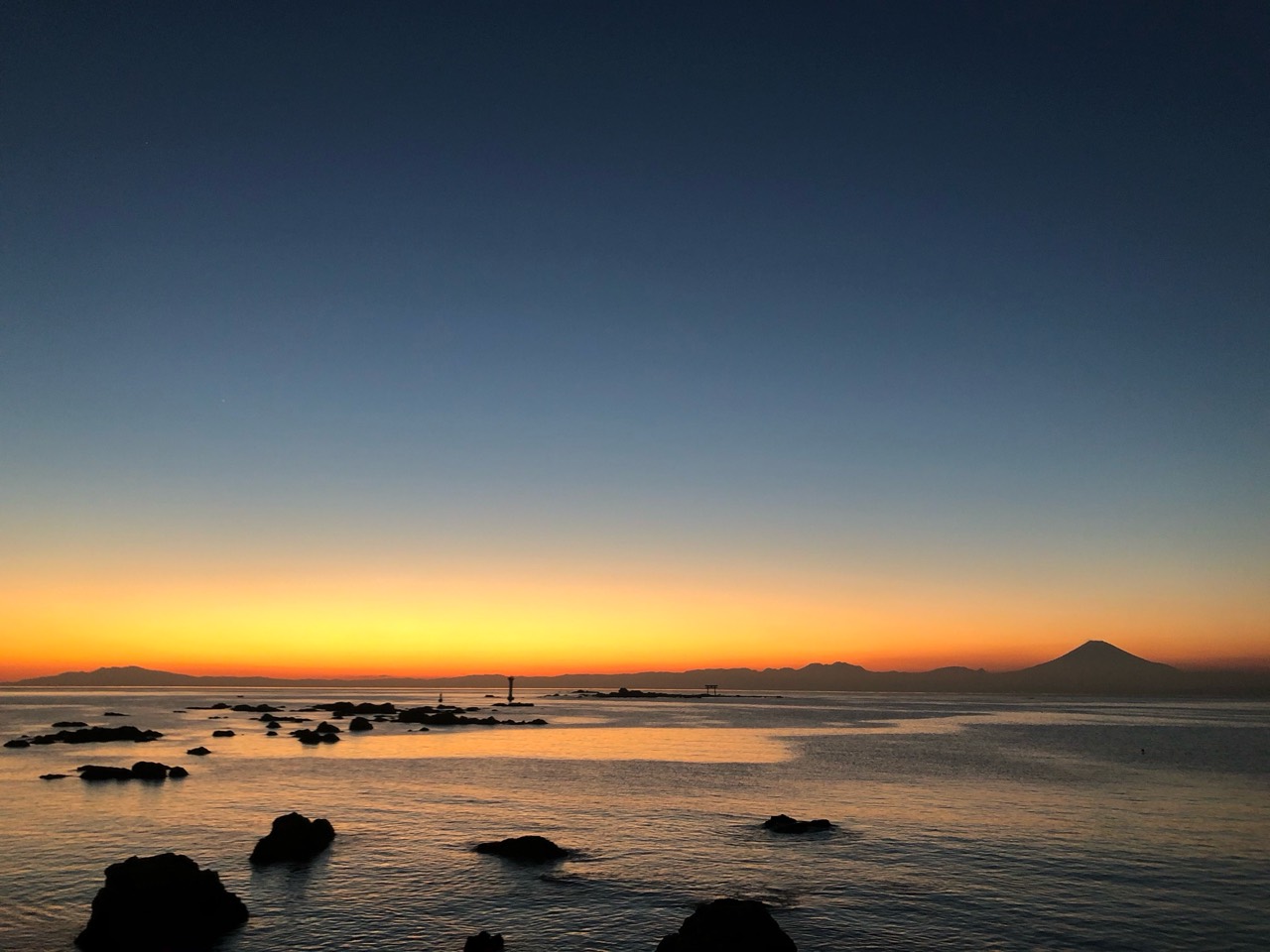 夕焼けが残る静かな海と、富士山のシルエット。