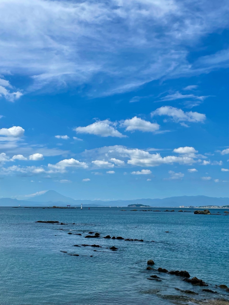 穏やかな海に続く岩と、遠くの富士山。